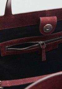 Bordeaux mockak läder handväska insida, med en dragkedjeficka, tryckknappslås och svart tygfoder. Slät textur, minimala hårdvarudetaljer.