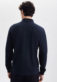 Polo a maniche lunghe in cotone blu navy, con colletto classico, orlo dritto e aperture laterali. Tessuto testurizzato con polsini a coste.