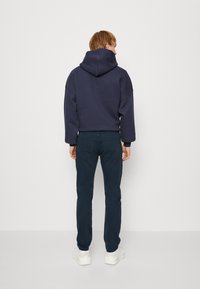 Tmavě modrá mikina s kapucí, volným střihem a velkou kapucí, doplněná tmavě modrými kalhotami a bílými teniskami. Jednoduchý design bez viditelných vzorů či log.