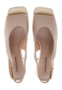 Talons hauts ouverts en cuir beige avec un talon bloc transparent, un design découpé et une bride à la cheville. Présente un embout métallique sur le bout.