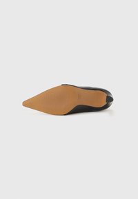Chaussure à talon haut noire avec un orteil pointu, un dessus lisse et une semelle en caoutchouc beige présentant un motif de grip texturé.
