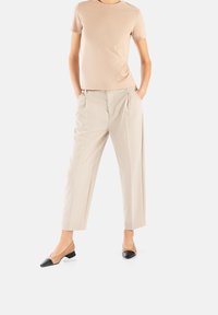 Beige Baumwoll-T-Shirt kombiniert mit gepolsterten, maßgeschneiderten cremefarbenen Hosen und schwarz-beigen, flachen Schuhen mit niedrigem Absatz, die eine strukturierte Silhouette schaffen.