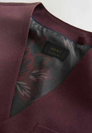 Sacou bordo care prezintă căptușeală interioară cu model floral și etichetă neagră NEXT cu textul „Made in Bangladesh”.