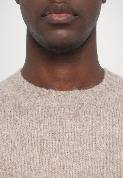 Maglione beige in lavorazione a maglia con texture a coste e colletto rotondo, caratterizzato da una superficie morbida e leggermente pelosa e una vestibilità comoda attorno al collo.
