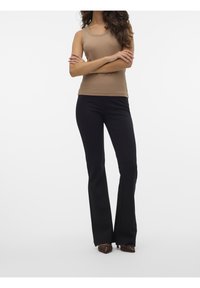 Débardeur beige côtelé associé à un pantalon noir évasé. Le pantalon présente une texture lisse et une coupe subtile. Chaussures marron à bouts pointus.