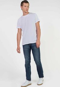Witte katoenen t-shirt, donkerblauwe spijkerbroek en witte sneakers. De outfit heeft een casual pasvorm en een minimalistisch ontwerp, zonder zichtbare patronen.