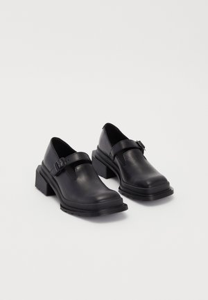 Black leather shoes with a rounded toe, flat sole, and a strap with a buckle detail. Chunky block heel for added stability.