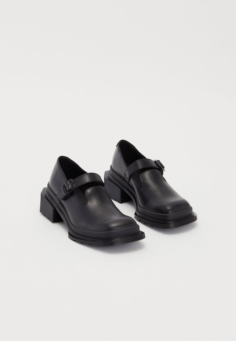 Black leather shoes with a rounded toe, flat sole, and a strap with a buckle detail. Chunky block heel for added stability.