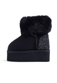 Stivaletto nero con morbida fascia in pelliccia, tomaia in suede elegante e pannello brillante testurizzato sul lato; suola piana piatta per maggiore comodità.
