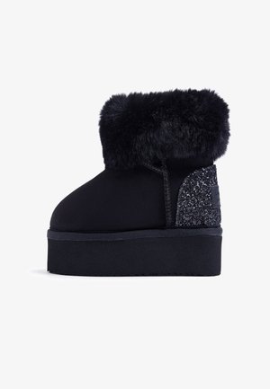 Bottines noires avec un doux revers en fourrure, dessus en daim lisse et panneau texturé scintillant sur le côté ; semelle plate pour plus de confort.