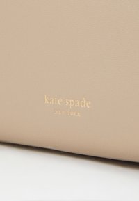 Beige leather with a textured finish featuring "kate spade NEW YORK" embossed in gold. Simple design, no additional patterns or accents.