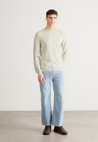 Világosszürke kötött pulóver kerek nyakkal és finom texturált mintákkal, világoskék bő szárú farmerrel és barna cipővel párosítva.