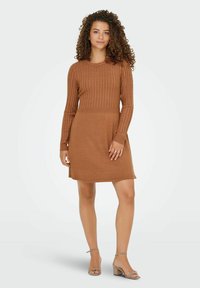 Pletena obleka v topli rjavi barvi, z rebrastim teksturiranim dolgim rokavom in telesom, gladko krilo ter stranskima razporkoma za lažje gibanje.