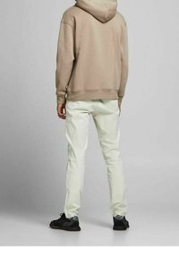Sudadera con capucha beige de corte relajado, combinada con pantalones verdes claros y zapatillas negras. El tejido parece suave y casual.
