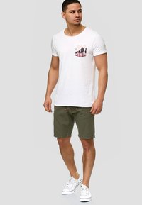 Hvid bomulds t-shirt med et pink palmetræ print på lommen, kombineret med olivengrønne shorts og hvide sneakers. Enkel og afslappet design.