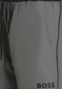 Sivé športové šortky s elastickým pásom a čiernym sťahovacím šnúrkou. Majú bočné vrecko a čierne logo na dolnej pravej nohe.