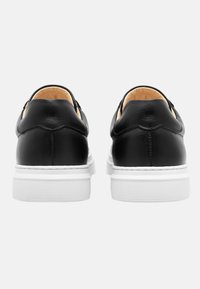 Black leather shoes featuring a smooth texture, white rubber soles, and a rounded toe design, with subtle stitching details at the back.