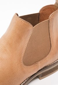 Botte Chelsea en cuir tanné avec panneau latéral élastique et semelle texturée, présentée en gros plan sur fond blanc.