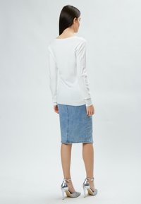 Pull blanc à manches longues avec une texture côtelée, associé à une jupe crayon en denim bleu clair et des chaussures à talons hauts argentées.