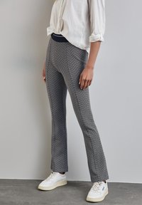 Zwart-wit gestreepte wijde broek met een elastische tailleband, gecombineerd met witte sneakers. De stof is gestructureerd en lichtgewicht.