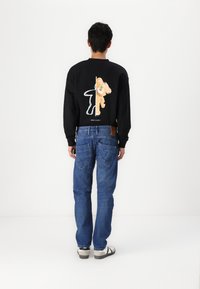 Black sweatshirt with back graphic, paired with blue baggy jeans. Material: cotton blend. Accents include printed design and blue tones.