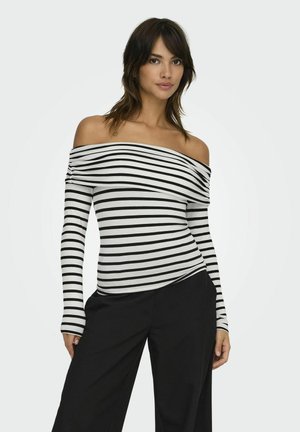 Haut à manches longues dénudant les épaules, avec des rayures horizontales noir et blanc, fabriqué dans un tissu doux. Associé à un pantalon noir ample.