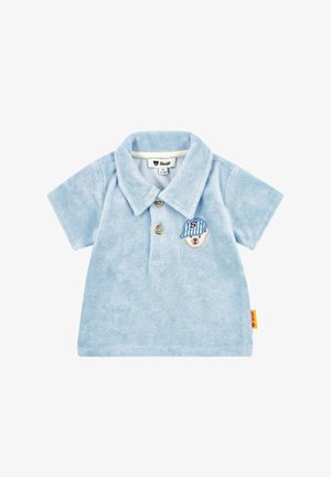 Polo de terciopelo azul claro con cuello, tres botones y un parche bordado de un oso con una gorra a rayas. Pequeña etiqueta de la marca en el lateral.