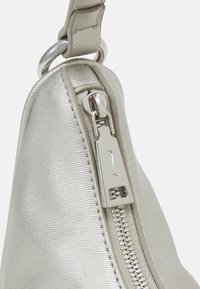 Gros plan sur une fermeture éclair de sac à main argenté texturé avec un tirette triangulaire arborant un symbole de point d'exclamation.