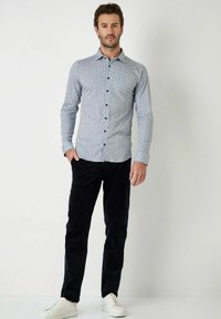  Lichtblauw overhemd met een geometrisch patroon, gecombineerd met donkerblauwe corduroybroek en witte sneakers.
