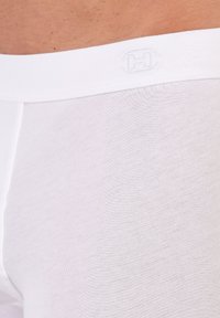 Vita bomullshorts med en slät yta, med ett enkelt elastiskt midjeband präglat med bokstaven "H."