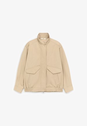 Smėlio spalvos bombonešio stiliaus striukė su stovinčiu apykakliu, spaustukais užsegami suktukai, elastine apačia ir dviem priekinėmis kišenėmis su atvartais ant balto fono.