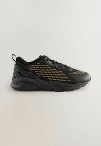 Schwarzer Sportschuh mit einem Obermaterial aus Mesh, das goldene Musterakzente aufweist, einer strukturierten Gummisohle und einer hinteren Zuglasche für leichtes Anziehen.