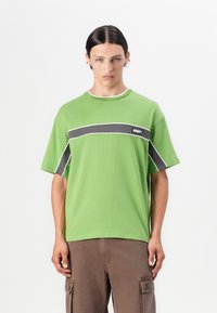 Green short-sleeve T-shirt in cotton, featuring a gray horizontal stripe and white piping, with a small black label on the chest.