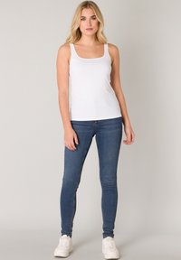 Witte tanktop met een vierkante halslijn, gedragen met donkerblauwe skinny jeans en witte sneakers. Soepele textuur en aansluitend ontwerp.