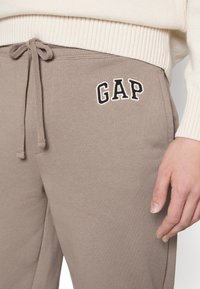 Tanfärgade bomullshuvtröjor har ett elastiskt midjeband med snöre, sidofickor och en broderad "GAP"-logotyp i marinblått på vänster lår.