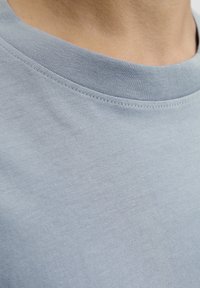 Close-up of a person's neck and light blue cotton crew neck shirt showing fabric texture and stitching details.