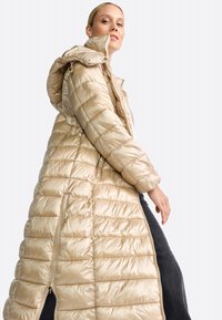 Lange, lichtbeige pufferjas met capuchon, met een doorgestikt ontwerp, ritszakken en een gladde, glanzende textuur.