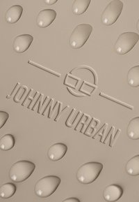 Beige szőnyeg, domborított vízcsepp mintázattal és "JOHNNY URBAN" logóval; sima textúra, lekerekített formák és minimalista tervezés.