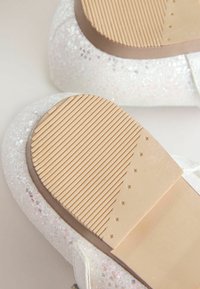 Scarpe bianche glitterate con suola in gomma testurizzata, caratterizzate da righe orizzontali e piccoli accenti a forma di stella vicino al tallone.