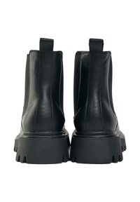 Black leather ankle boots with elastic side panels, ribbed texture, and thick rubber soles featuring a serrated edge. Two pull tabs at the back.