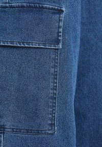 Pantaloni cargo in denim di un blu scuro, con una grande tasca laterale, cuciture spesse e una consistenza liscia.