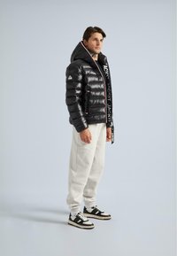 Jachetă puf cu guler înalt, textură lucioasă și detalii cu logo contrastant. Purtați-o peste pantaloni de trening crem și adidași negri.
