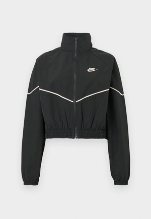 Schwarze kurze Jacke mit hohem Kragen, Reißverschluss, elastischem Bund und weißen Paspelierungen. Mit Nike-Logo auf der Brust.