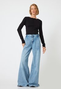 Zwarte top met lange mouwen en een geschulpte halslijn, gecombineerd met lichtblauwe denim jeans met een hoge taille en zichtbare stiknaden.