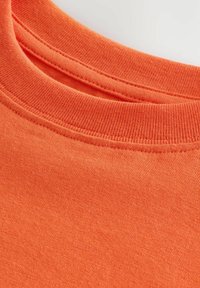 T-shirt à manches courtes et col rond en tissu orange vif à la texture lisse et au col cousu, présentant un design décontracté.