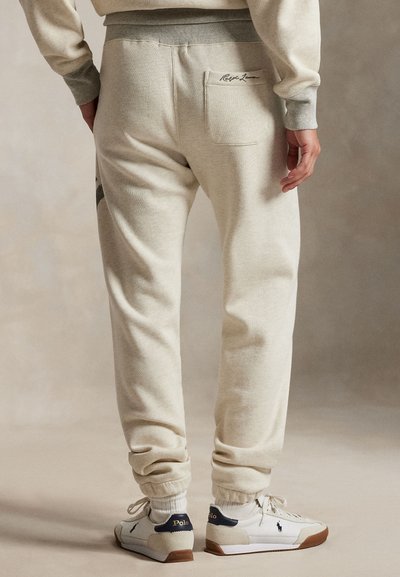 Lyse beigefargede joggebukser med ribbestrikkede mansjetter og linning. Har en baklomme med logo og en avslappet passform. Matt stofftekstur.