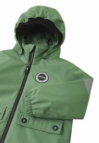 Giacca impermeabile verde con cappuccio, polsini elasticizzati, chiusura con zip e due tasche frontali. Presenta un patch con logo e accenti riflettenti.