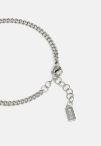 Bracciale in metallo argento con maglie intrecciate, dotato di chiusura a molla e di un'etichetta rettangolare incisa con la scritta "BOSS."