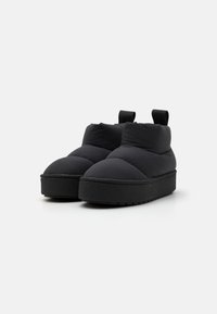 Sorte polstrede slip-on-sko med rund tå, forhøjet platformsål og trækstropper på bagsiden for nem påklædning. Glat tekstur overalt.