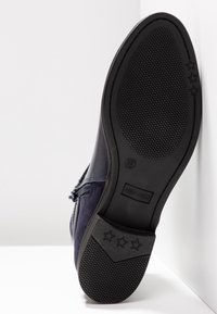 Semelle d’une botte noire affichant une adhérence texturée, marque ANNA FIELD, taille 37, avec des motifs d’usure en forme d’étoile sur le talon et la semelle.